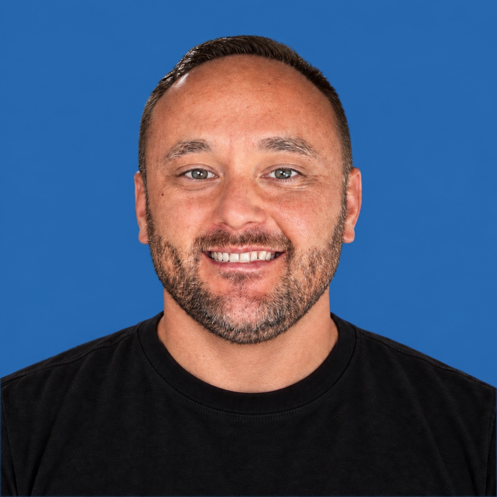 Kyle Newsom smiling in a black T-shirt against a blue background